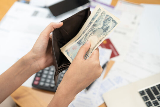 Close up of a person hands taking out banknotes, cash or money from a leather wallet while calculating home budget, planning expense and doing personal finance management.