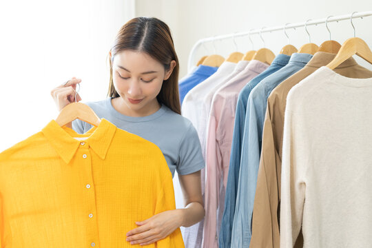 Choose clothes to wear, attractive asian young woman, girl try on appare, happy choice of shirt, female outfit on hanger in wardrobe in room closet at home. Deciding blouse what to put on which one