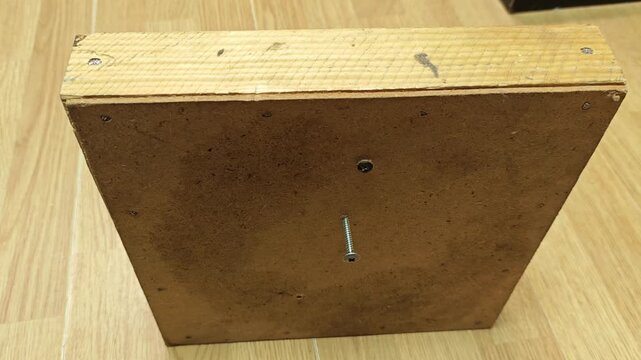 Furniture panel assembly work with visible screw hardware on wooden surface. Board stays in place while fastener and predrilled holes suggest careful fitting during furniture construction.
