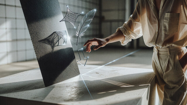 Hand reaches toward glowing white icons of a feather, arrow, and mesh plane floating above a dark carbon fiber panel in an industrial studio setting with bright sunlight.