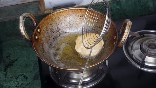 Indian cuisine frying cooking puri or poori or Luchi in hot oil on fire gas stove in home kitchen.