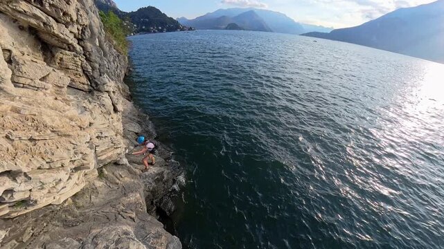View of a female climber traversing Via Ferrata Morcate on Lake Como cliff at sunset, Italy