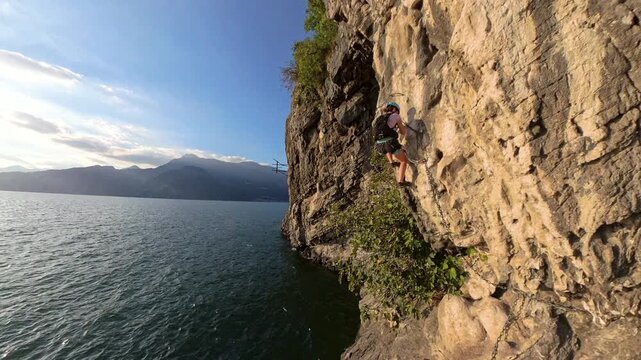 Female climber traversing Via Ferrata Morcate on Lake Como cliff at sunset, Italy
