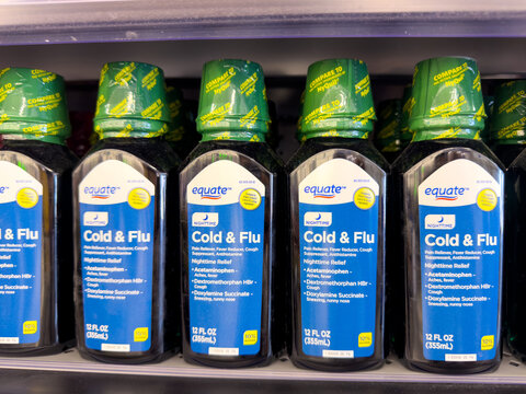 Frisco, Texas, USA - August 31th, 2026: Equate cold and flu liquid bottles standing with green caps in row on dark rack in Walmart pharmacy shelf
