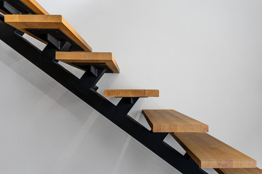 Open wood and metal staircase on white wall. Minimal interior design with copy space.