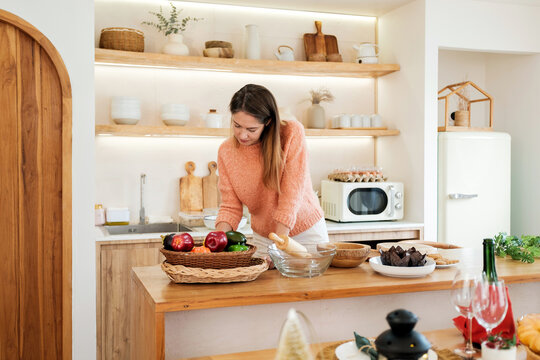 Woman prepares fresh vegetables at a wooden kitchen counter in a bright modern home, creating a warm everyday scene focused on healthy cooking, fresh ingredients, and meal preparation.