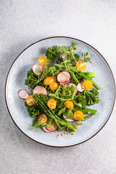 Grilled green spring vegetables: radish, tomato, broccolini on stone background.