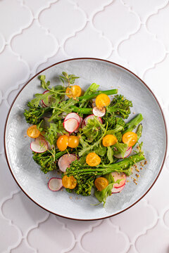 Grilled green spring vegetables: radish, tomato, broccolini on stone background.