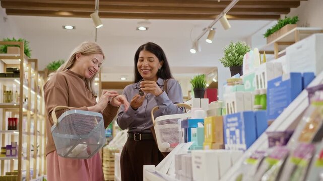 Diverse women testing organic cosmetic serum on hand while shopping in eco store with baskets. Ideal for retail skincare commercials, natural cosmetics ads, beauty product marketing