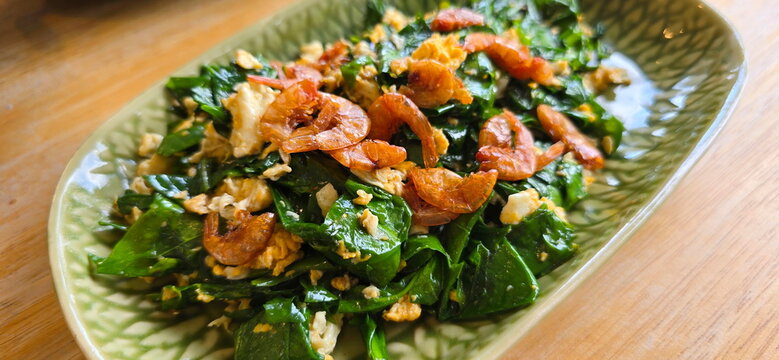 Stir-fried Melinjo leaves with egg, dried shrimp, served on green plate. This is healthy dish featuring. Gnetum gnemon var. tenerum leaves. Popular local dishes of Southern Thailand. Family: GNETACEAE