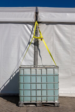 Detail of Large IBC Water Container Secured with Ratchet Straps on a White Event Tent Under Blue Sky