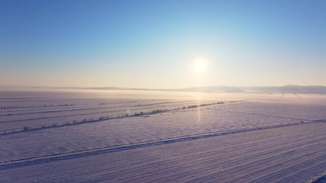 Aerial View of Snow-Covered Agricultural Fields at Sunrise with Mist