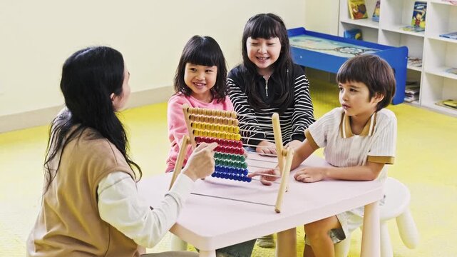 Teacher and three children use a colorful abacus at a classroom table, practicing counting and math in a bright, playful preschool setting.