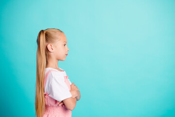 Young girl in profile portrait with long ponytail wearing pink dress against a bright blue studio background, thoughtful side view of a child showing confidence and calm expression © deagreez