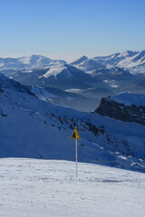 Ski safety warning sign stands on a snowy mountain slope overlooking dramatic alpine peaks near Morzine Avoriaz in the French Alps, France. © Tatiana
