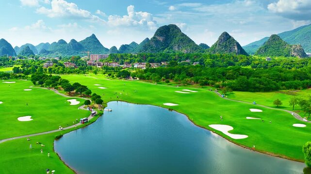 Lush green golf course with a blue pond and paths, framed by karst mountain peaks under bright sunlight in Guilin, China.
