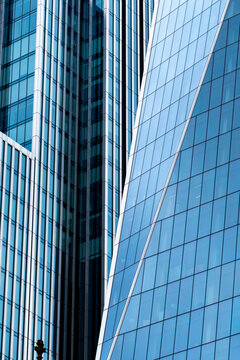 Blue glass skyscraper facades forming a narrow urban canyon with reflective architecture and a pedestrian providing human scale in a modern city scene