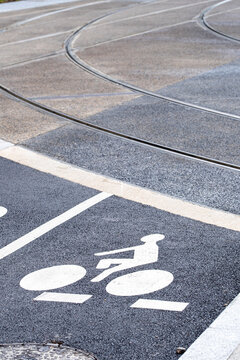 Urban bicycle lane with white cycling symbol beside curved tram tracks and road markings showing shared mobility in a modern city setting