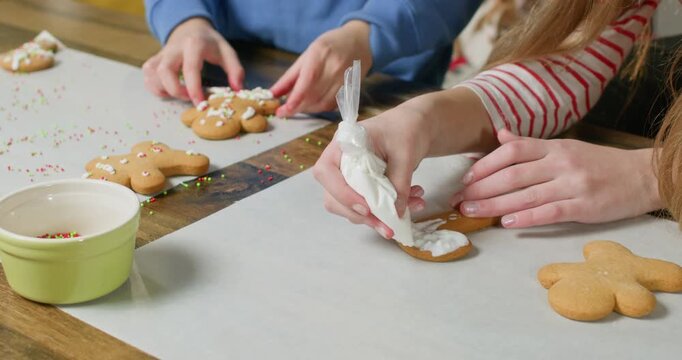 Children are making Christmas gingerbread cookies on the kitchen table, decorating them with icing and sprinkling them with colorful beads.