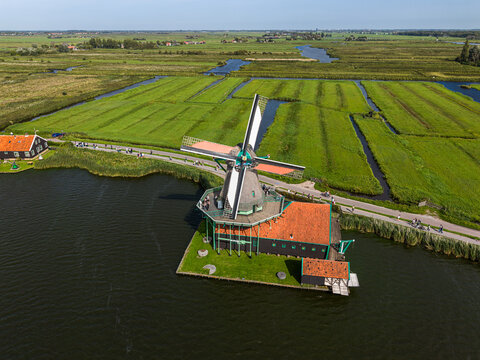 High angle vertical aerial drone photograph of De Kat historic dye windmill, river Zaan, polder drainage canals, and walking path in Zaanse Schans, Zaandam, North Holland, Netherlands on sunny day