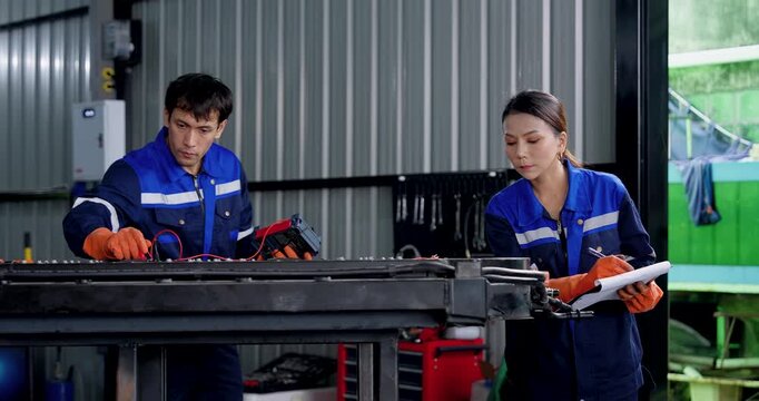 EV battery diagnostics by two technicians testing exposed battery pack with meter probes and checking readings in modern automotive workshop, supporting professional electric vehicle maintenance.