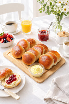 Freshly baked homemade scones or buns served on a wooden board with butter, strawberry jam, coffee, orange juice, and fresh berries for breakfast. Cozy morning aesthetic table setting.
