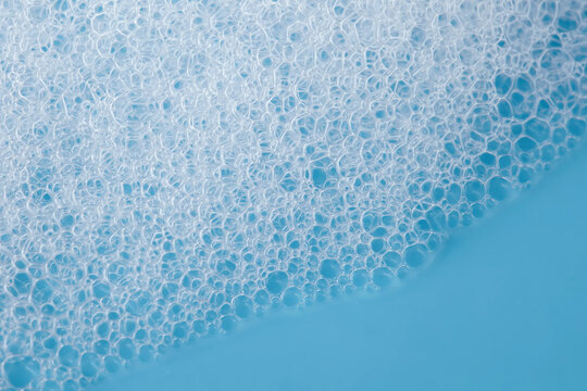 Soap bubbles suds close-up on blue background. Shampoo bubbles, cleaning supplies concept. Soapy white foam texture up view. Shallow depth of field. selective focus