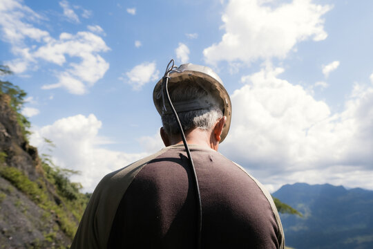 Miner wearing hard hat outdoors looking at mountains