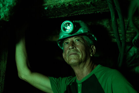 Miner wearing hard hat and headlamp in dark underground shaft