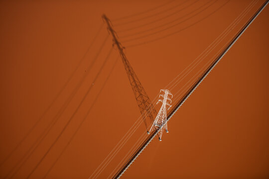 Aerial view of a high-voltage electricity pylon casting a long shadow over the reddish-brown landscape of the San Francisco Bay Area in Newark, California, United States.