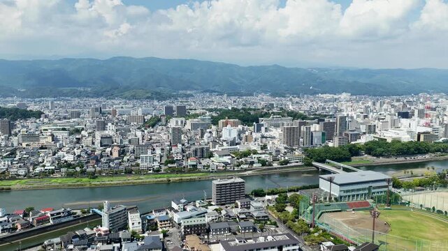 Aerial drone footage over urban cityscape with river and mountains in Kochi, Japan