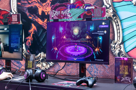 Cologne, Germany - August 26, 2026: Gaming setup featuring a monitor displaying Grim Rival game, headphones, and promotional materials in a vibrant exhibition space
