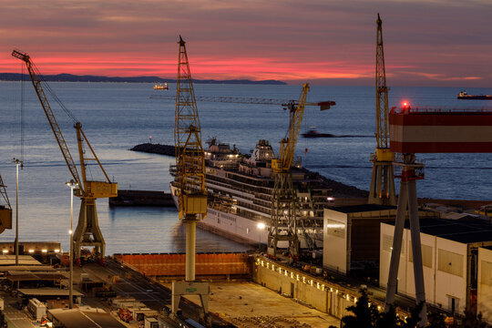 Aerial view of Ancona Port at sunset with large industrial cranes and a cruise ship docked in the harbor under a vibrant sky Ancona, Marche, Italy.