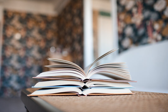 Stack of open paper boos on rattan table in living room close up. Reading hobby.