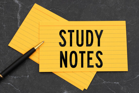 Study Notes text on a bright yellow index cards with pen on black stone