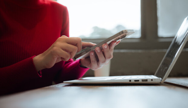A close-up shot of a young woman using a smartphone alongside a laptop, reflecting mobile technology, digital communication, remote work, and productivity in the modern business world.