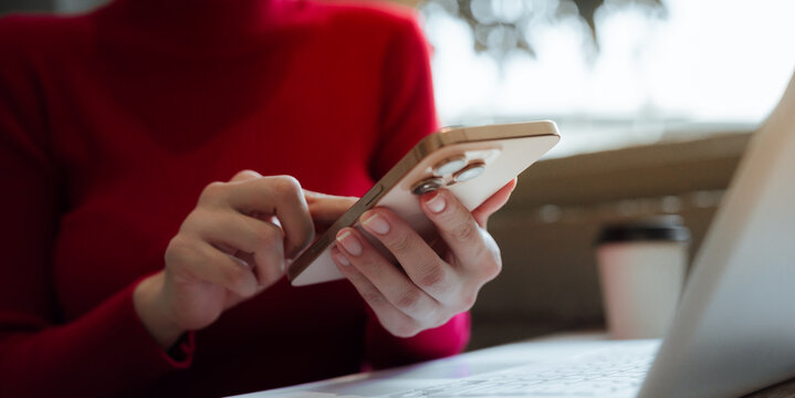 A close-up shot of a young woman using a smartphone alongside a laptop, reflecting mobile technology, digital communication, remote work, and productivity in the modern business world.
