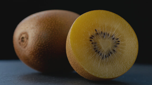 Macro shot of a ripe golden kiwi cut in half with a heart-shaped core, rich juicy pulp and seeds on a dark background with a blurred whole kiwi for healthy eating, gourmet food, and culinary content.
