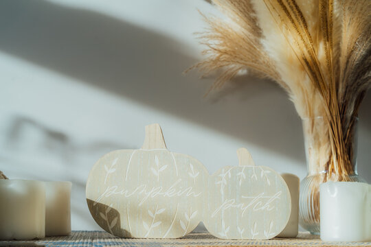 Cozy warm autumn home interior - white knitted pumpkins, wooden statuette, candles, dried flowers on the wooden console with white wall background. Scandinavian minimalist hygge home fall decor.