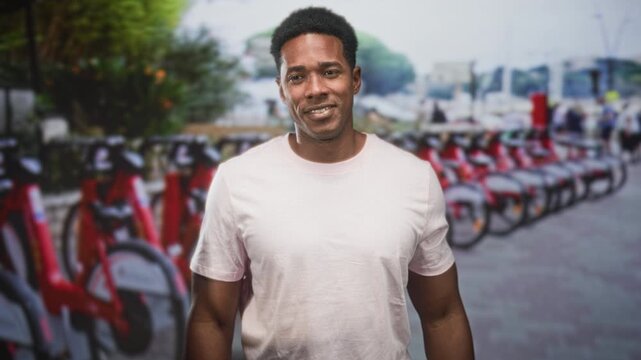Man points with both hands toward a row of red rental bicycles at a street bike share station while smiling; urban mobility confidence.