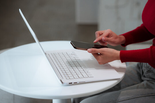 A close-up shot of a young woman using a smartphone alongside a laptop, reflecting mobile technology, digital communication, remote work, and productivity in the modern business world.