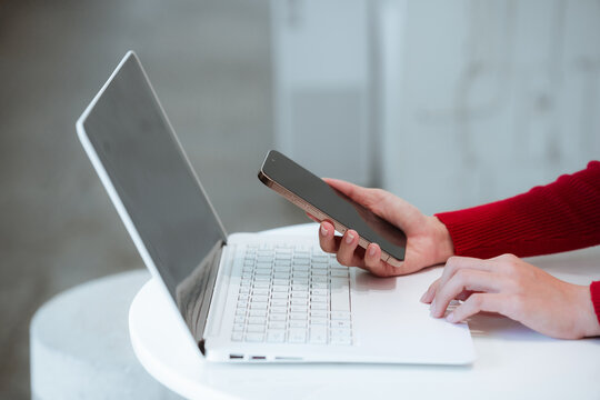 A close-up shot of a young woman using a smartphone alongside a laptop, reflecting mobile technology, digital communication, remote work, and productivity in the modern business world.
