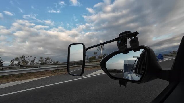 Car towing a caravan on the highway reflected in side mirror