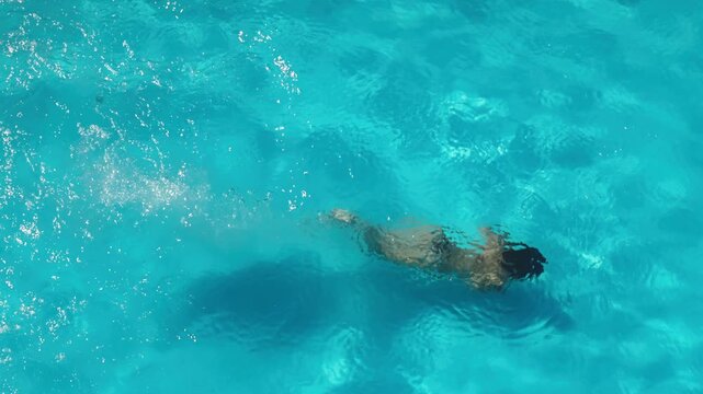 Woman swimming underwater in a bright blue pool, creating bubbles and water movement. Swimming, fitness and summer recreation concept.