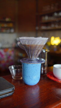 Freshly brewed pour over coffee dripping through a glass filter into a blue ceramic mug in a cozy cafe setting
