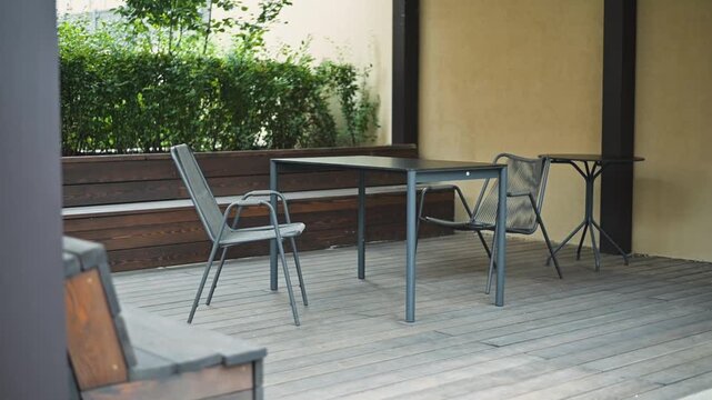 patio with a table and chairs, all made from metal and positioned on wooden flooring. Surrounding vegetation provides some shade and texture to the setting