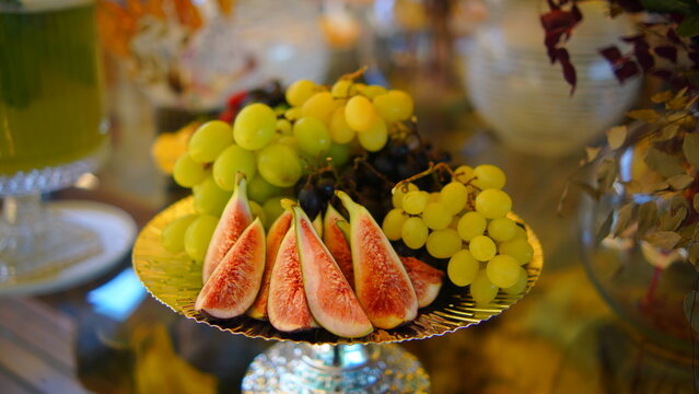 Elegant arrangement of fresh sliced figs and green grapes on a silver pedestal stand for a luxury event buffet