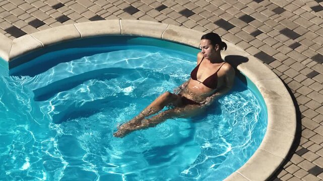 Woman relaxing in a small swimming pool, leaning near the edge and enjoying refreshing water. Summer vacation and resort lifestyle concept.
