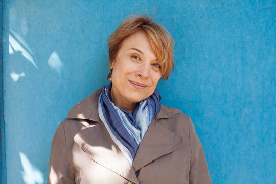 Portrait of mature woman with short hair standing outdoors against blue wall background