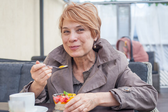 Cute senior woman eating dessert while sitting in city street cafe